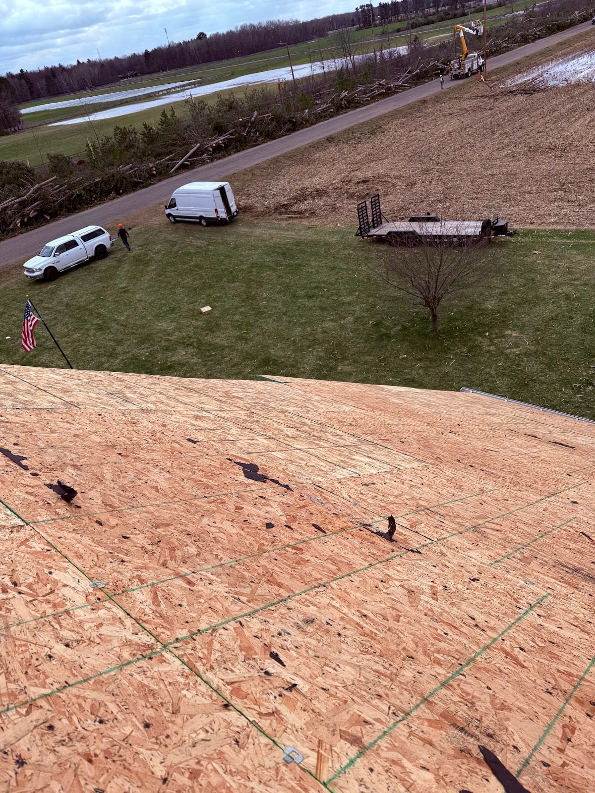 New roof decking going down after a storm tear-off, with crew trucks staged below.