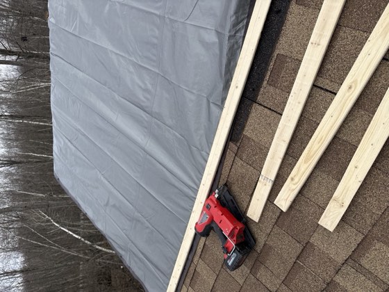 New lumber and decking secured over a tarped roof during a rebuild.