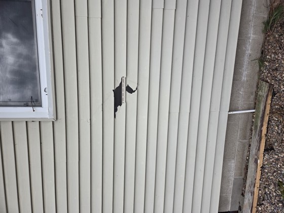 Storm impact damage to a home's vinyl siding and window.